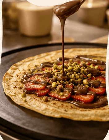 Chocolate poured over a fresh crepe with strawberries and pistachio